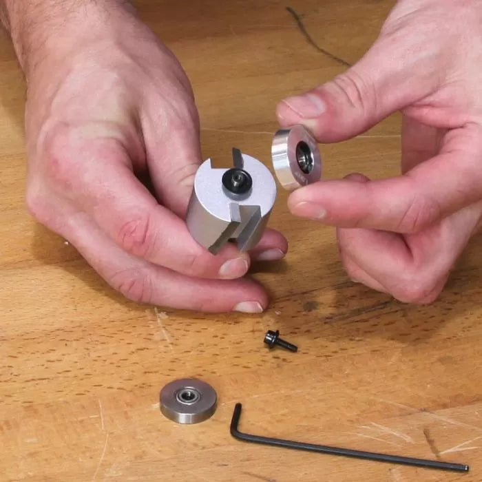 Hands assembling woodworking router bit with bearings and hex key on wooden workbench