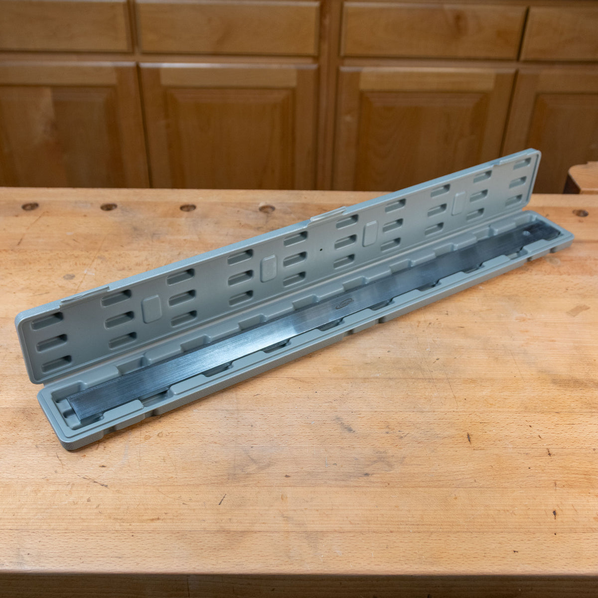 Woodworking planer blade in a gray storage case on a workshop bench