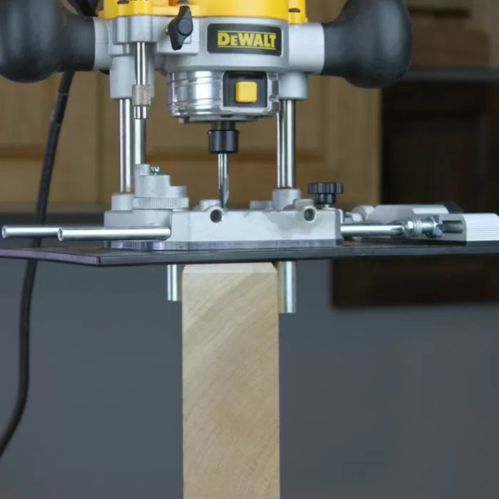 Plunge router with edge guide cutting a square wood post in a woodworking workshop.