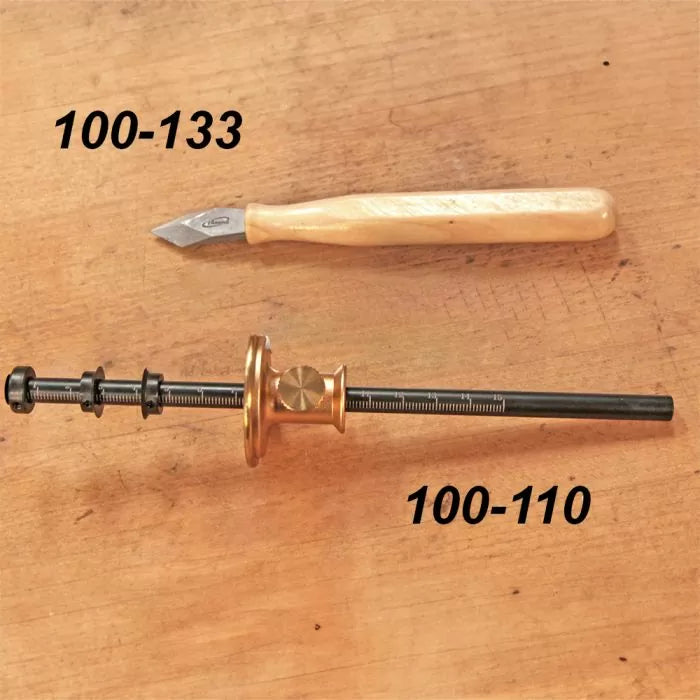 Woodworking marking knife and marking gauge on wood surface, labeled 100-133 and 100-110.