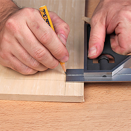 Hand using a combination square and pencil to mark precise lines on a wood board