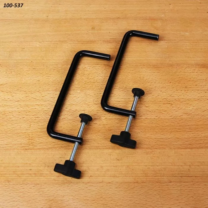 Pair of black steel woodworking table clamps on a wooden surface