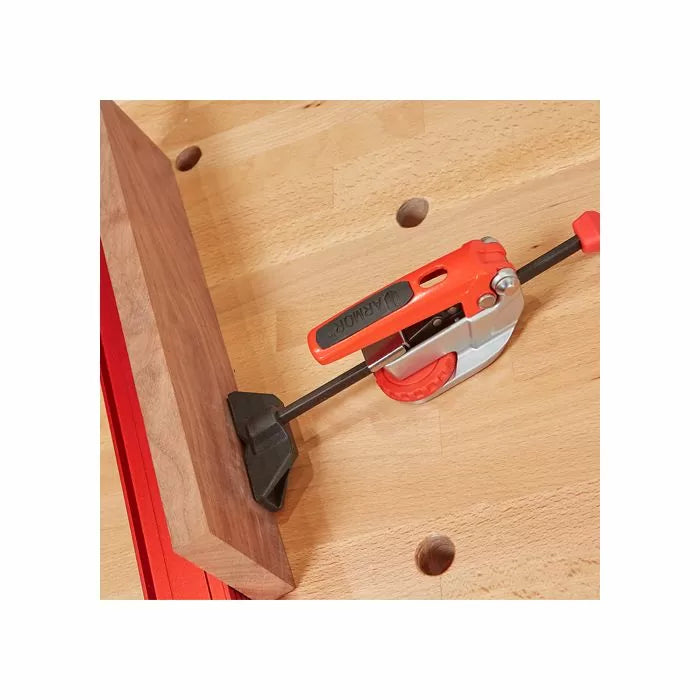 Woodworking quick clamp securing a board on a workbench with dog holes