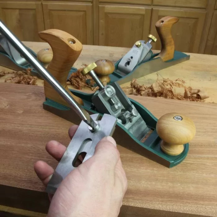 Hand adjusting woodworking hand plane tool on wooden workbench with wood shavings