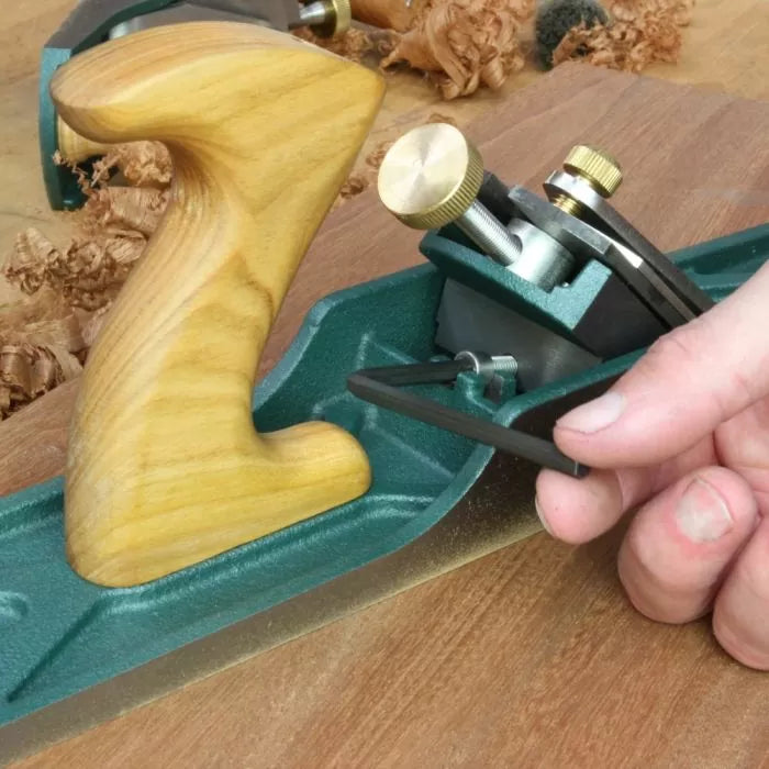 Hand adjusting bench plane woodworking tool on wood surface with shavings