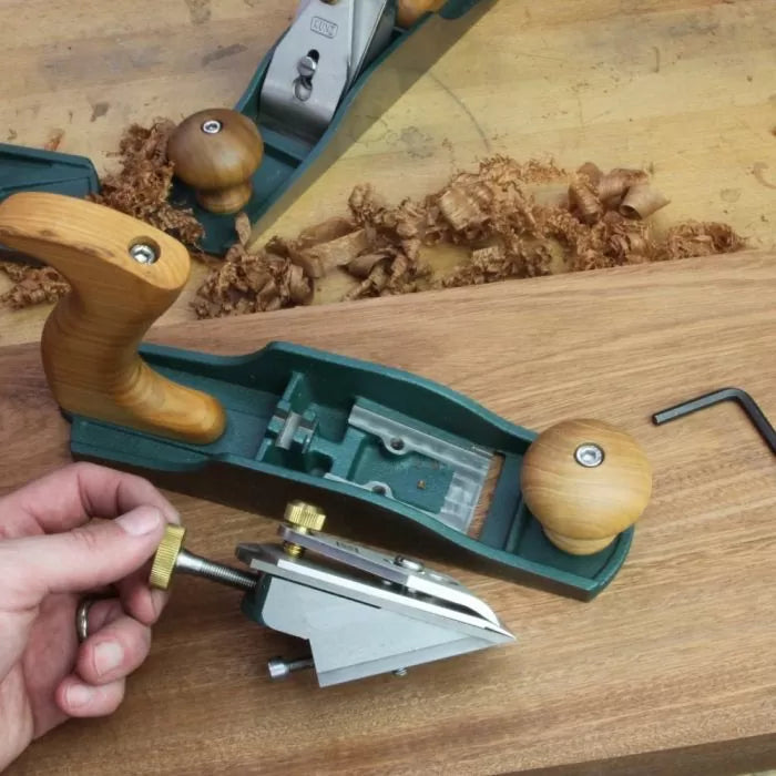 Woodworking hand plane with frog mechanism removed on workbench, wood shavings visible