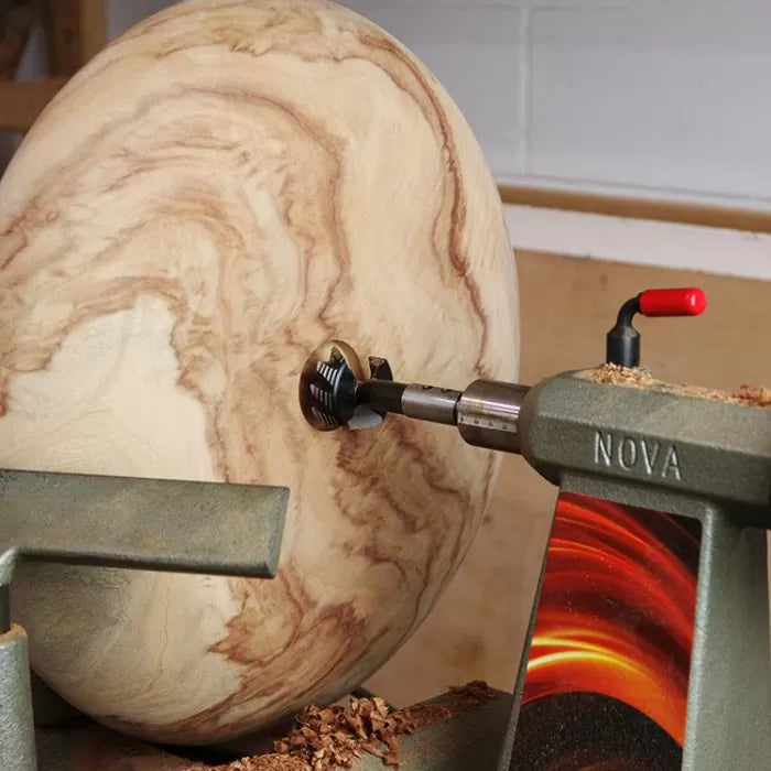 Wood lathe shaping a large round wood blank with spiral bit in woodworking workshop