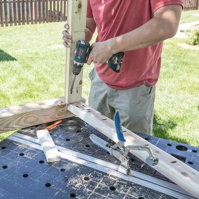 Person using cordless drill and pocket hole jig on wood boards at outdoor workbench