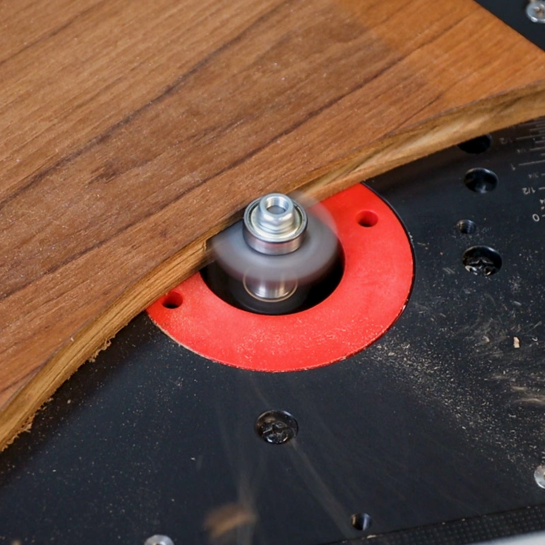 Woodworking router table trimming curved wood edge with router bit and red insert ring.