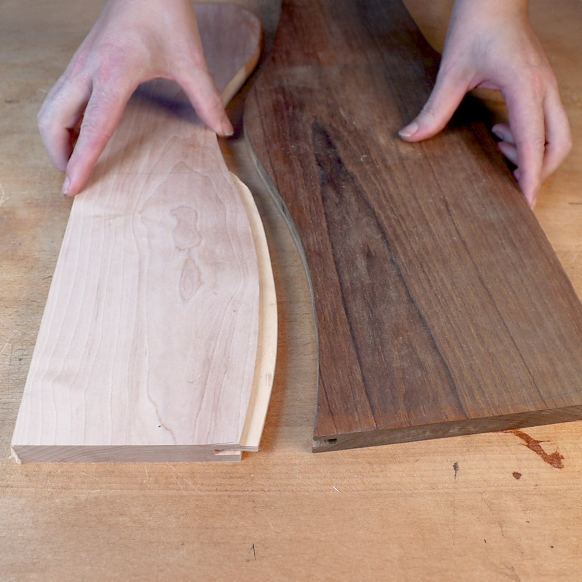 Hands aligning curved wooden boards on a workbench for woodworking project