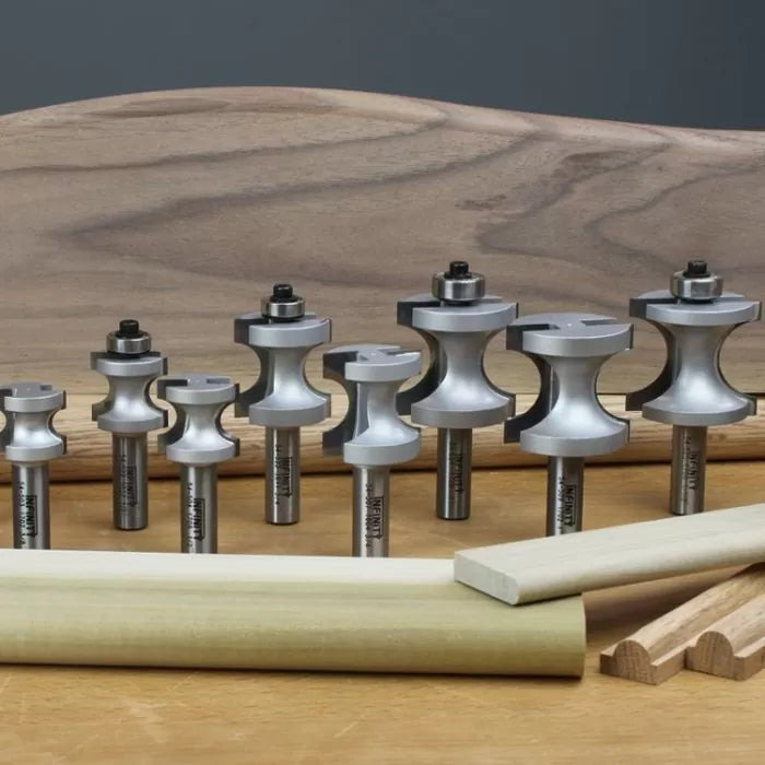 Set of woodworking router bits on a workbench with sample wood moldings
