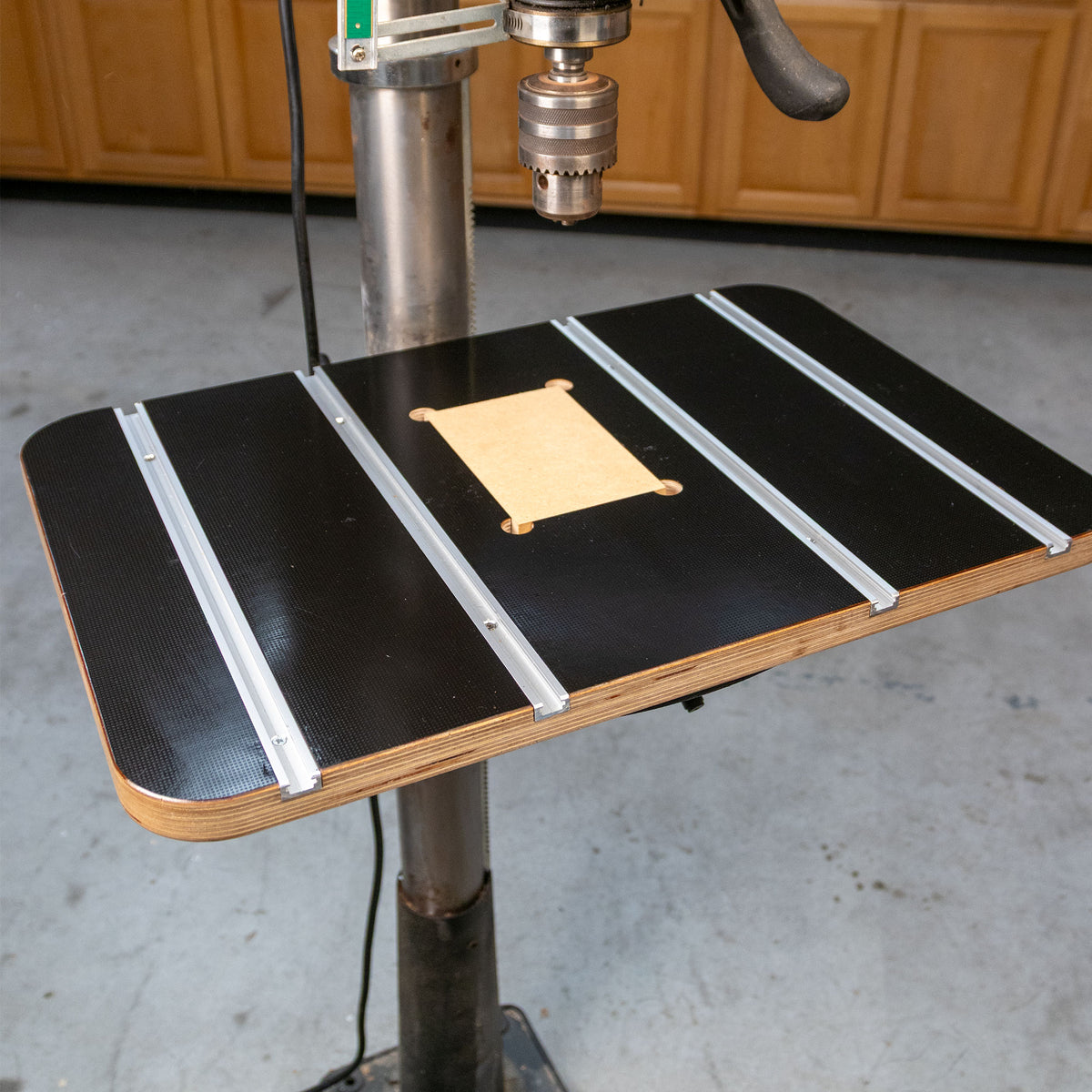 Drill press table with T-tracks and insert for woodworking, mounted in a workshop