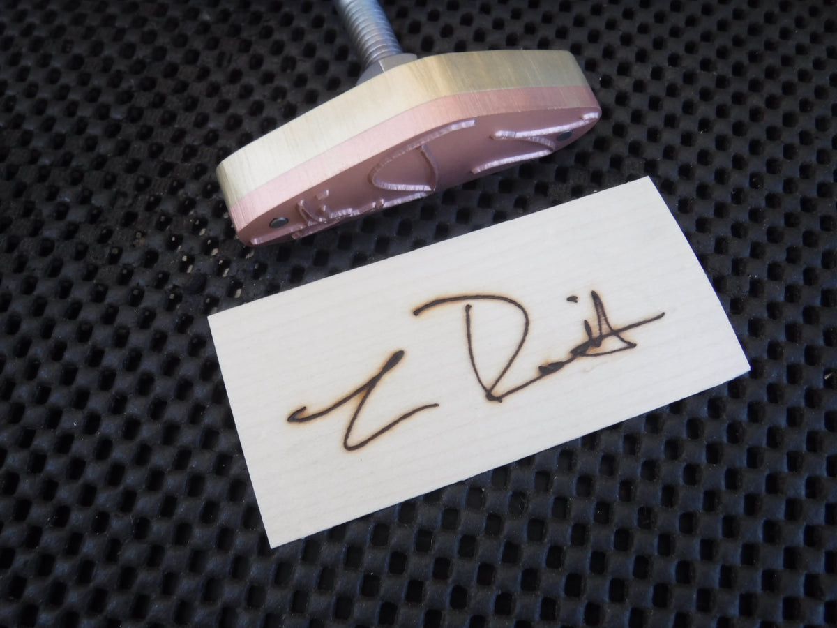 Signature branding iron with engraved custom wood burn mark on light wood piece