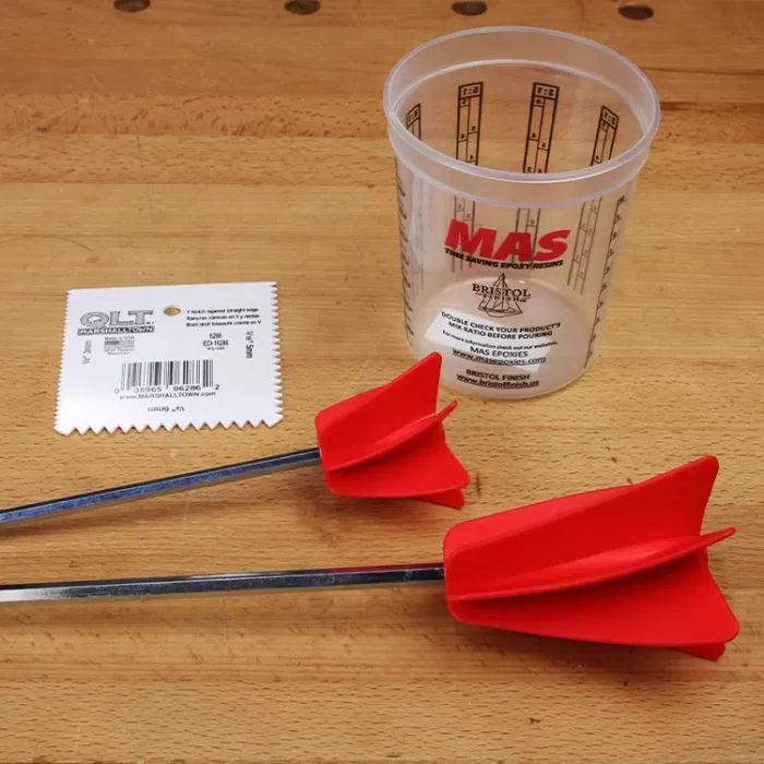 Woodworking epoxy mixing accessories with plastic cup, red paddles, and notched spreader on workbench.