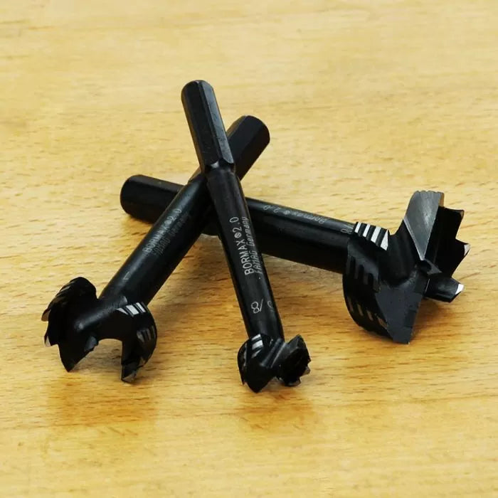 Three black forstner drill bits for woodworking on a light wood surface
