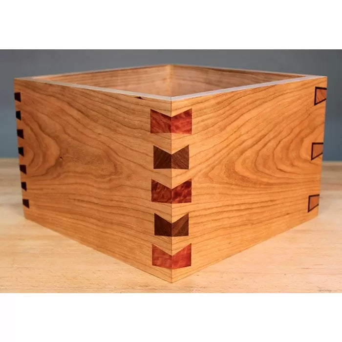Handcrafted wooden box with decorative dovetail joints on a workbench, woodworking project.