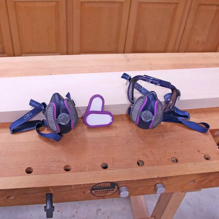Woodworking dust masks, safety goggles, and a filter on a workbench in a woodshop setting.