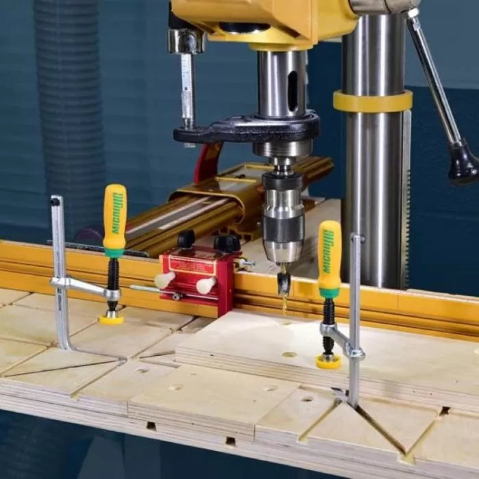 Drill press using woodworking jig system with clamps on a workbench, precision drilling setup.