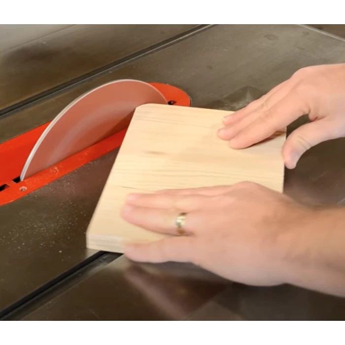 Cutting a wooden board on a table saw with hands guiding the wood for precise woodworking.