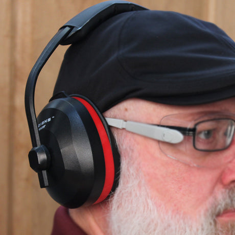 Man wearing black over-ear hearing protection earmuffs and safety glasses