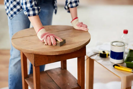 Person in work gloves sanding the top of a worn wooden side table