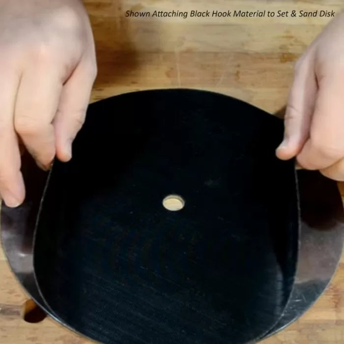 Hands attaching black hook material to a sanding disk on a wooden workbench.