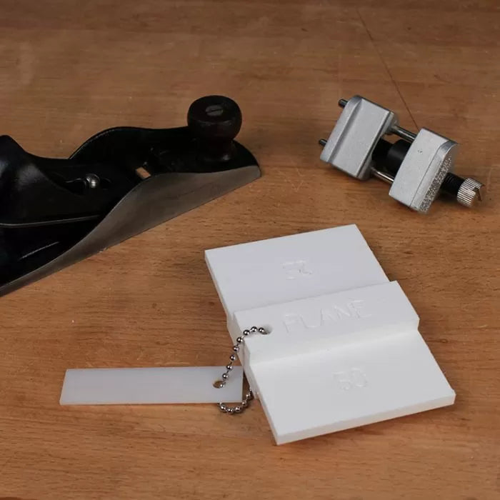 Woodworking hand plane, honing guide, and plastic angle gauge on a wooden workbench.
