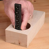 Measuring hole depth in wood block with a black precision ruler on a woodworking bench