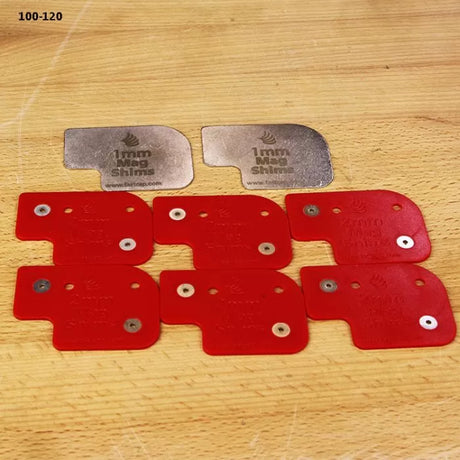 Set of red and silver 1mm magnetic shims on wood surface for woodworking tool setup