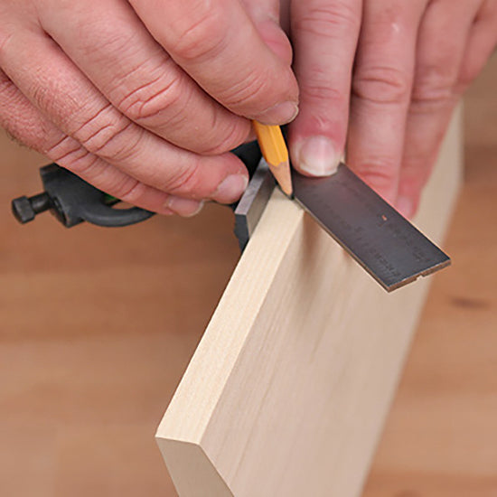 Woodworker using a combination square and pencil to mark a straight line on a wood board