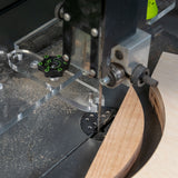 Bandsaw cutting curved wood with clear fence system and dust on table