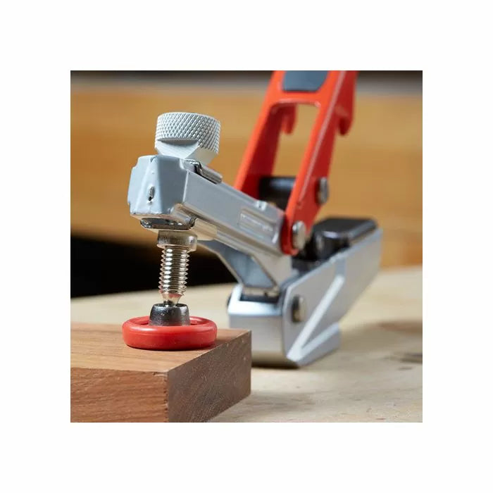 Toggle clamp with red handle securing wood on workbench, woodworking tool close-up