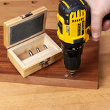 Cordless drill driving screw into wood near a box of woodworking drill bits on workbench
