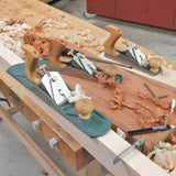Bench planes with wood shavings on a woodworking workbench, showing hand tools in use.
