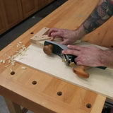 Woodworker using a hand plane on a shooting board at a woodworking bench.