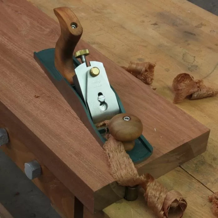 Hand plane smoothing wood board on workbench with wood shavings, woodworking tool