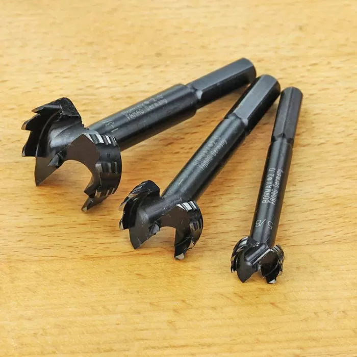 Three black forstner drill bits for woodworking on a wooden surface
