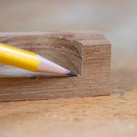 Yellow pencil pointing at precise curved groove cut in wood block, woodworking detail