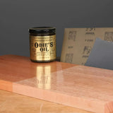 Odie's Oil wood finish jar on a polished wood board with sandpaper sheets