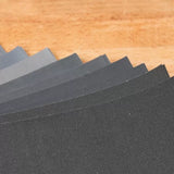 Assorted abrasive sandpaper sheets fanned out on a wooden surface for woodworking