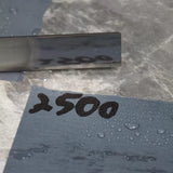 Wet 2500 grit sharpening stone with water droplets and polished tool blade, woodworking tool accessory