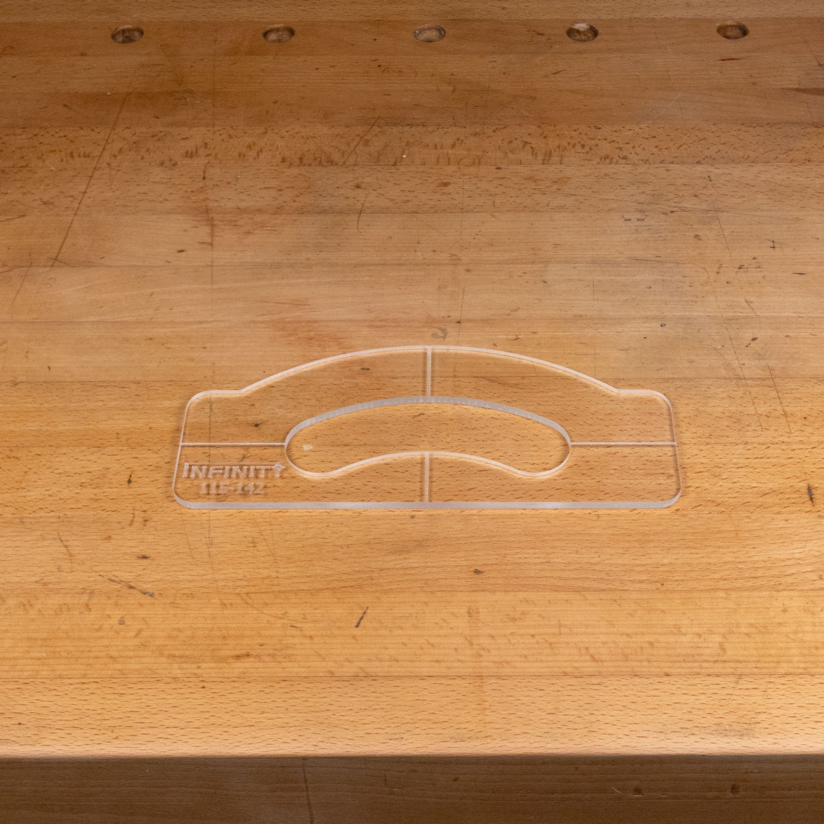 Clear acrylic handle template for woodworking placed on a wooden workbench.
