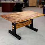 Live edge hardwood table with black metal legs in a woodworking shop setting