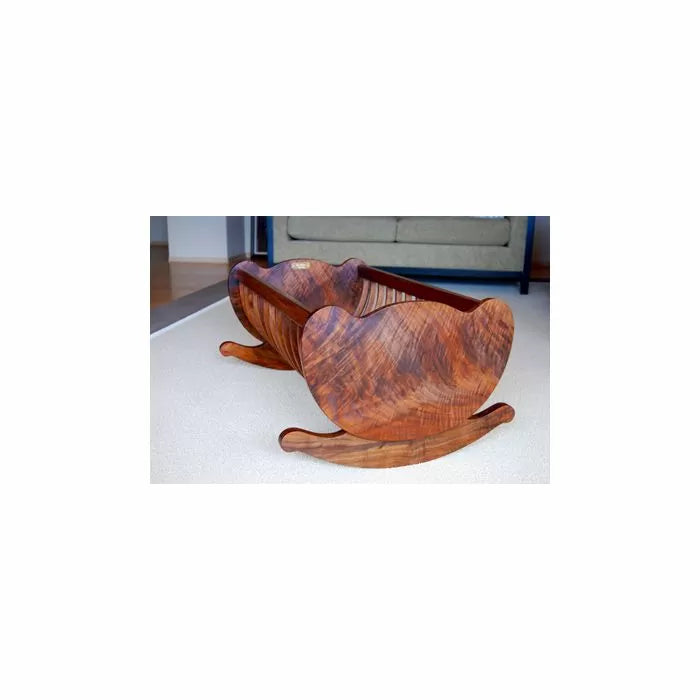 Handcrafted wooden rocking cradle with curved sides on a carpeted floor