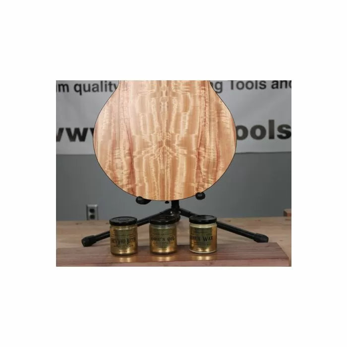 Curly maple guitar body on stand with three wood finishing products on workbench