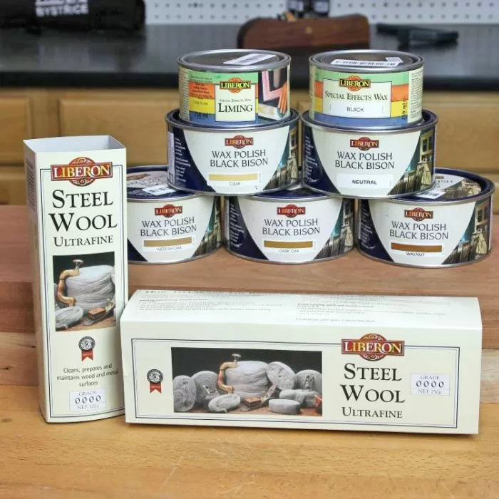 Liberon steel wool and various Black Bison wax polish tins for woodworking on a workbench