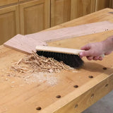 Hand sweeping wood shavings and sawdust off a woodworking bench with a brush