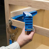 Person using a blue pocket hole jig tool with clamp on a wooden cabinet frame.