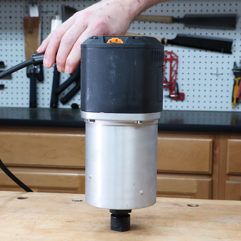 Hand holding woodworking router motor on workbench in workshop setting