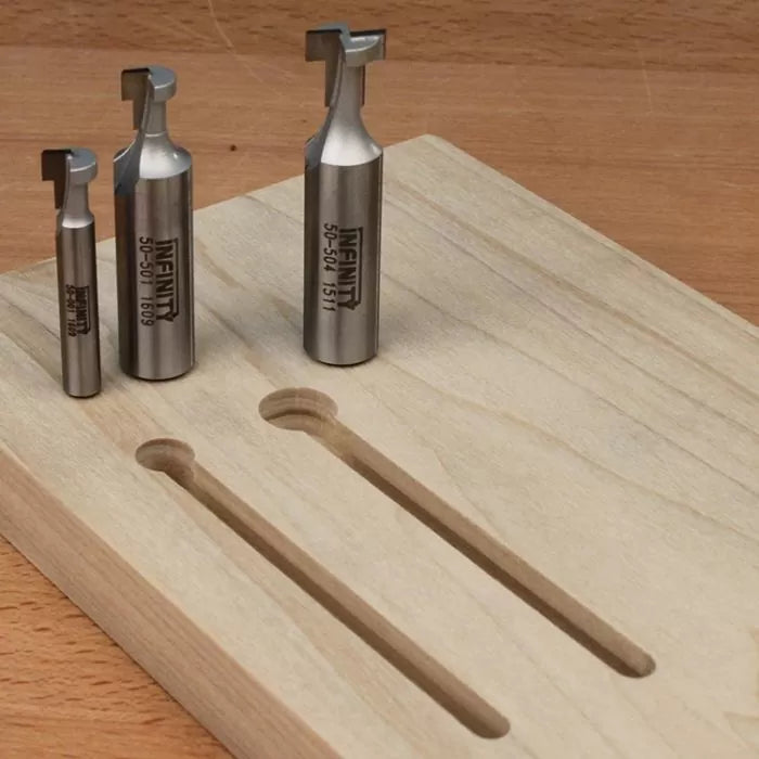 Three metal woodworking router bits next to a wooden board with dado grooves on a workbench.